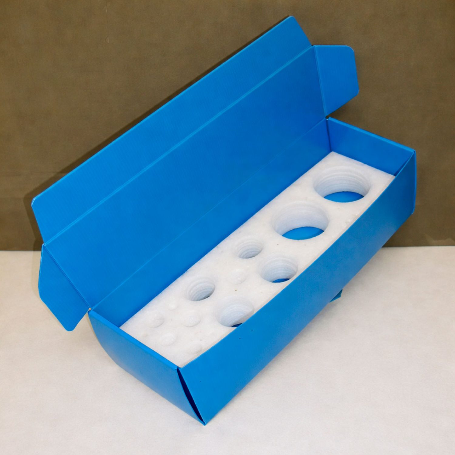 Caja de cartón plástico de polipropileno celular con interior de espuma troquelada, diseñada para proteger y organizar piezas delicadas durante el transporte.