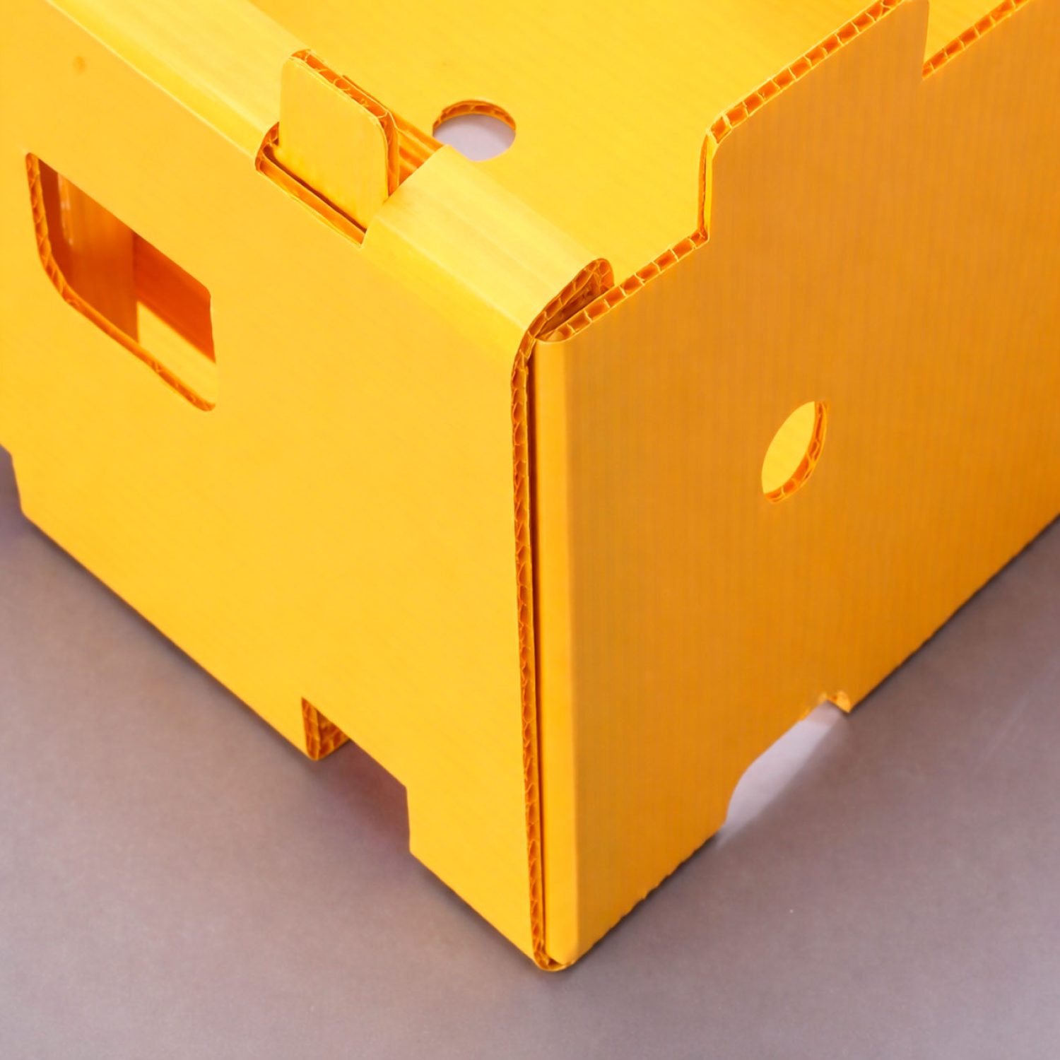 Caja de cartón plástico de polipropileno celular en color amarillo, resistente y reutilizable, con asas troqueladas para transporte y almacenamiento.