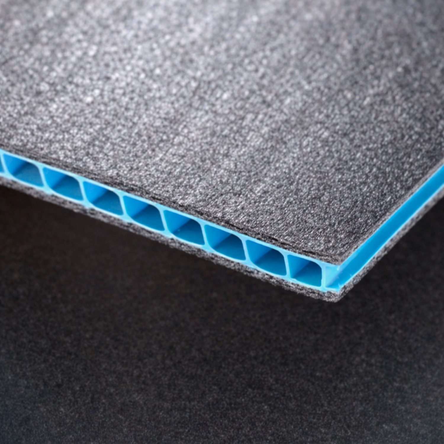 Plancha de cartón plástico alveolar con núcleo celular y acabado gris, ligera y resistente.