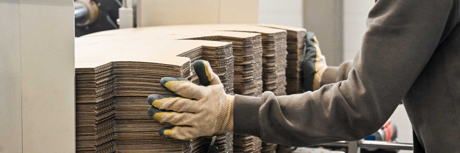 Operario manipulando troqueles de cartón en máquina industrial de fabricación de embalajes.