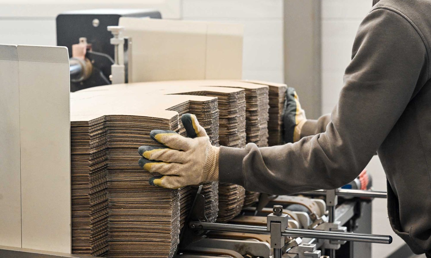 Operario manipulando troqueles de cartón en máquina industrial de fabricación de embalajes.